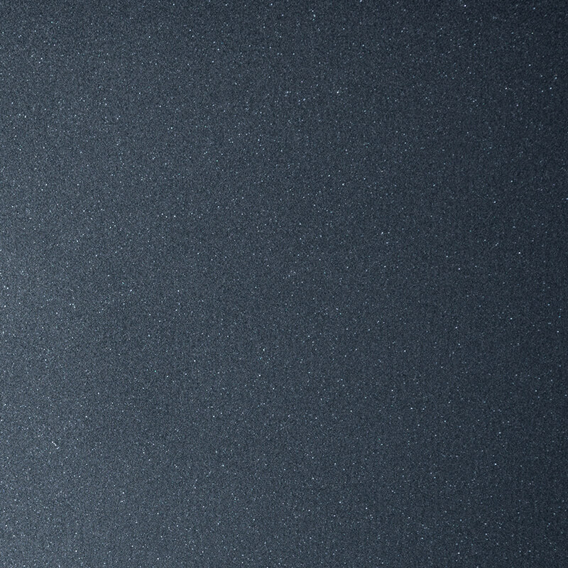 A close-up image of a dark, textured surface with a subtle sparkle, resembling black sandpaper or a finely grained metallic material. The surface appears rough and slightly reflective.